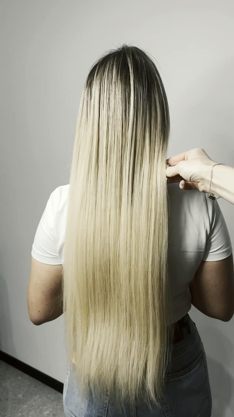 Dlhé hladké blond vlasy po predĺžení, pohľad zozadu; majsterka ich prečesáva (video bez zvuku)